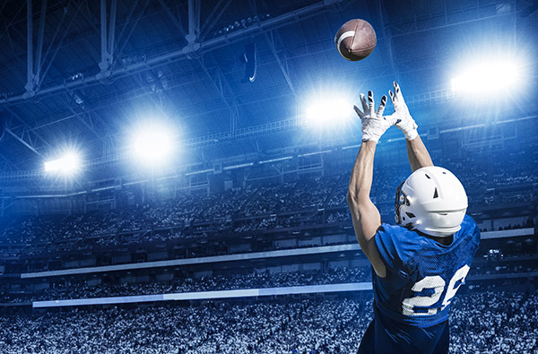 Alt text: packed stadium at nighttime with an American football player catching the ball in the foreground